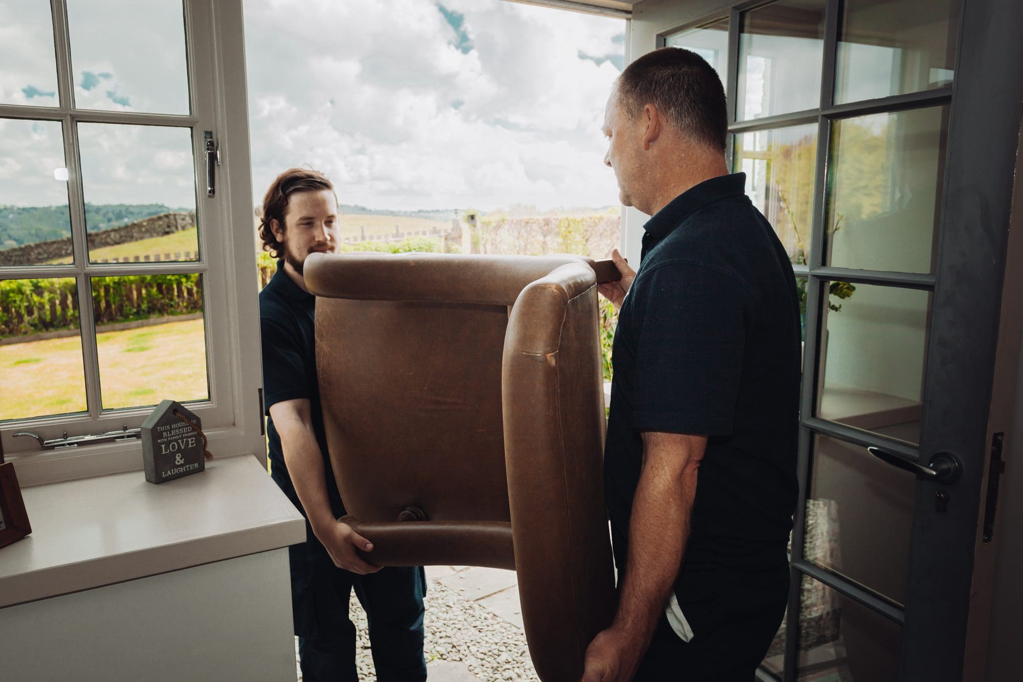two men carrying a sofa chair at the door going outside.