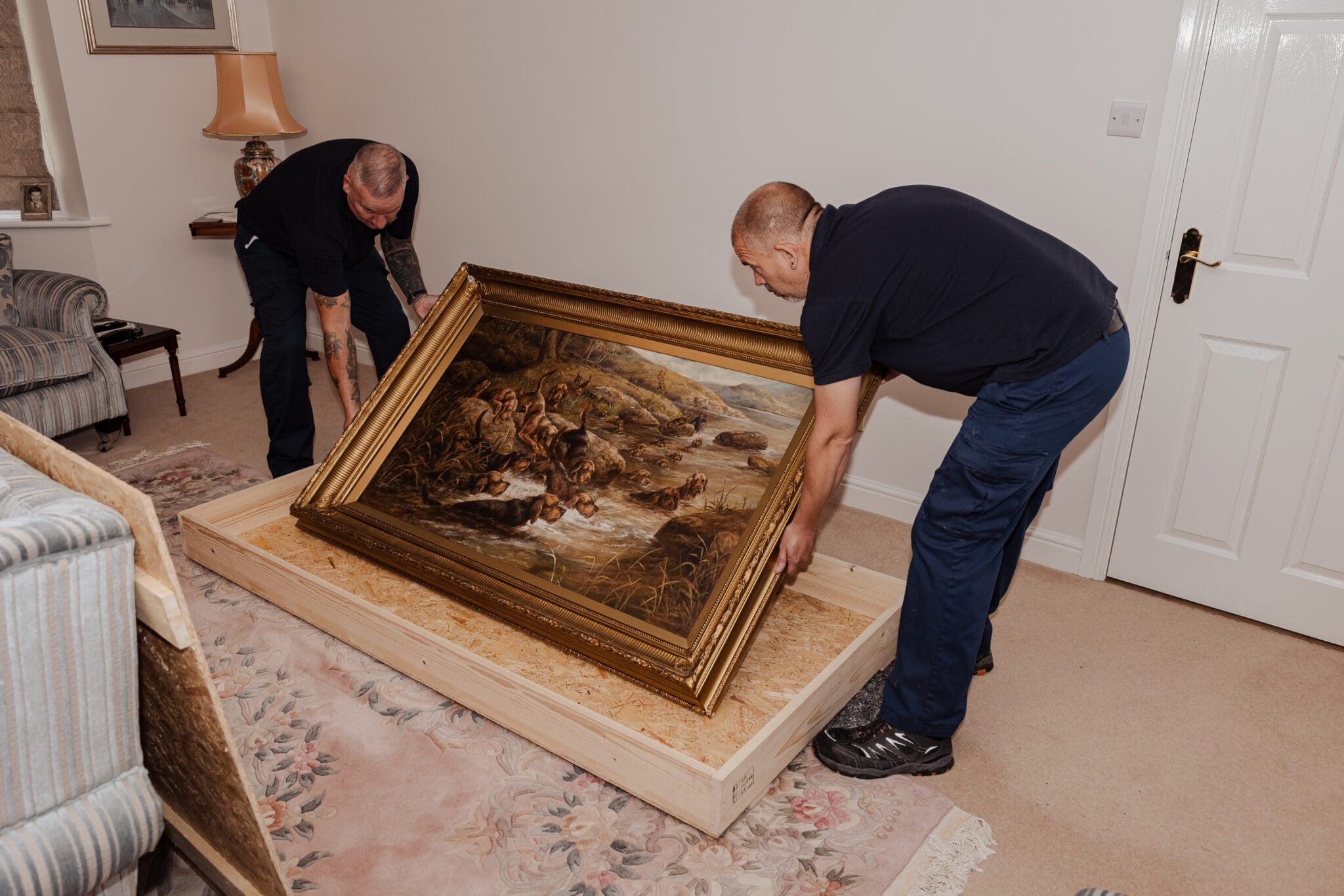 two men carefully carrying a big wall picture frame into a wooden crate