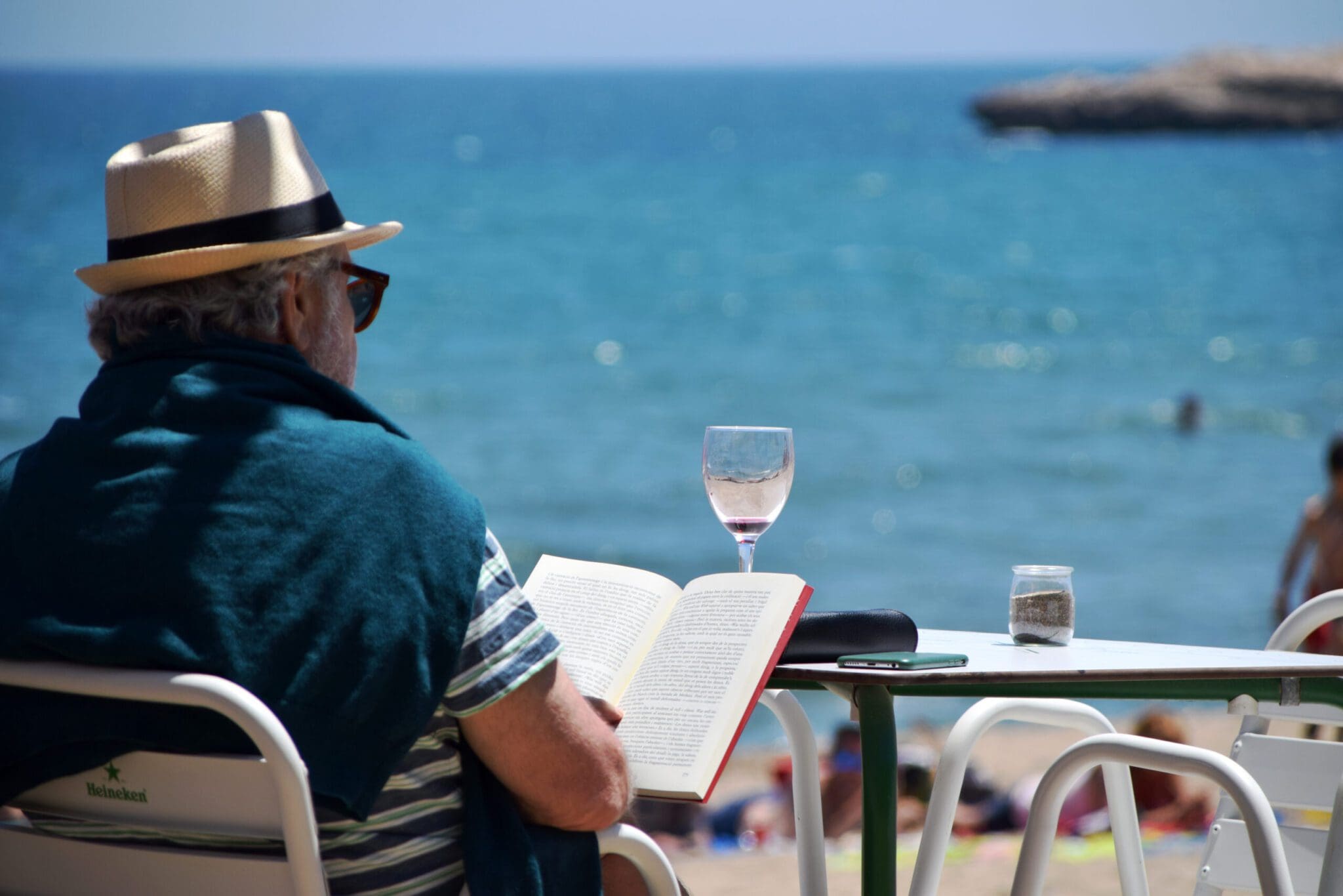 a man reading a book on a beach with a glass of drink